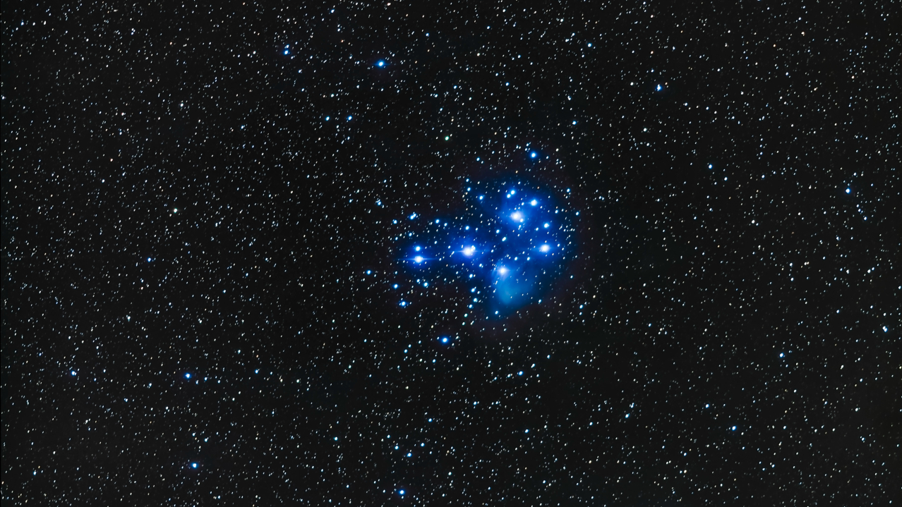 The blue-white stars of the Pleiades open cluster shine in a dark night sky.
