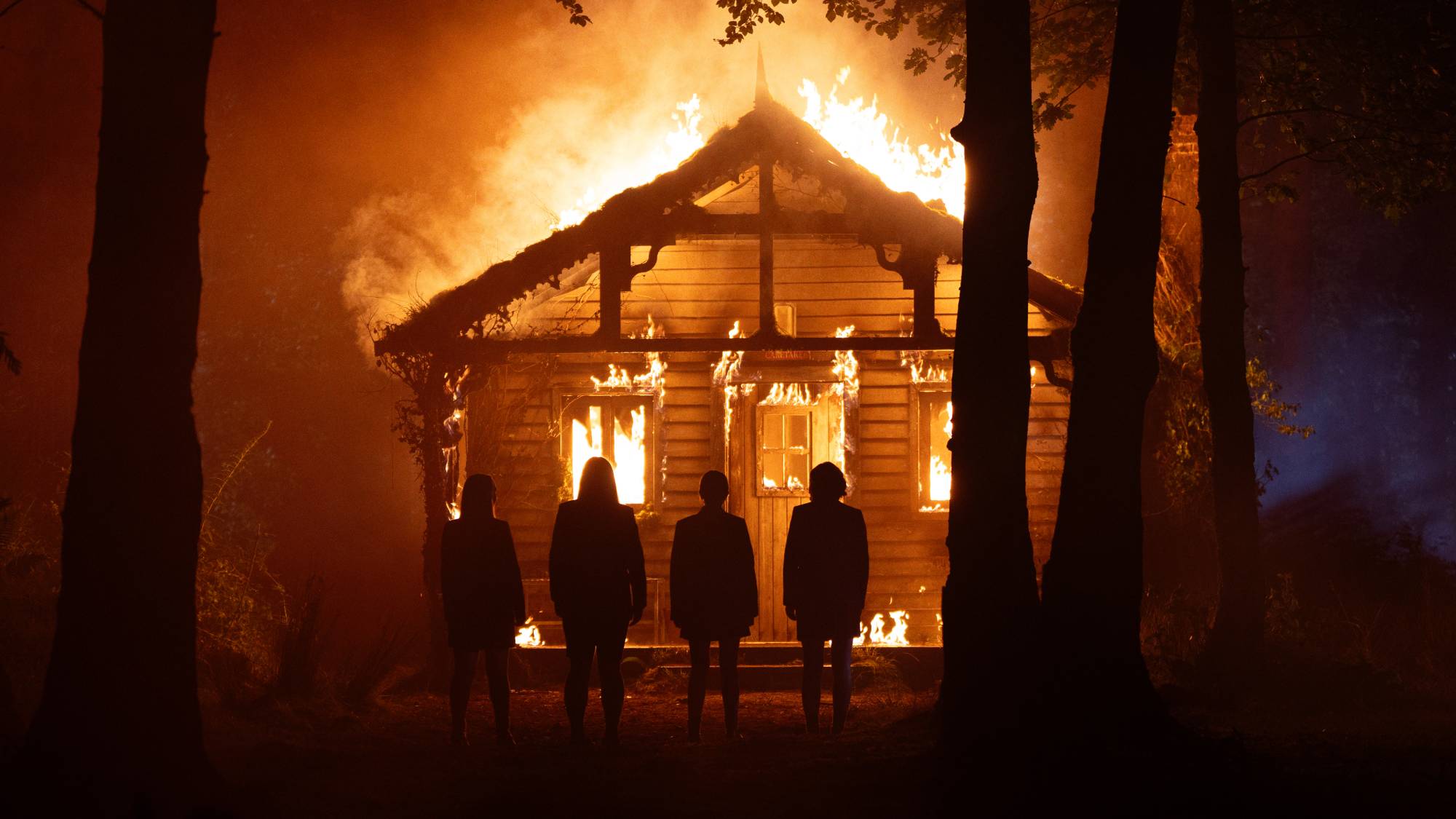 Scene from "How to Get to Heaven from Belfast" on Netflix showing a house on fire in the woods