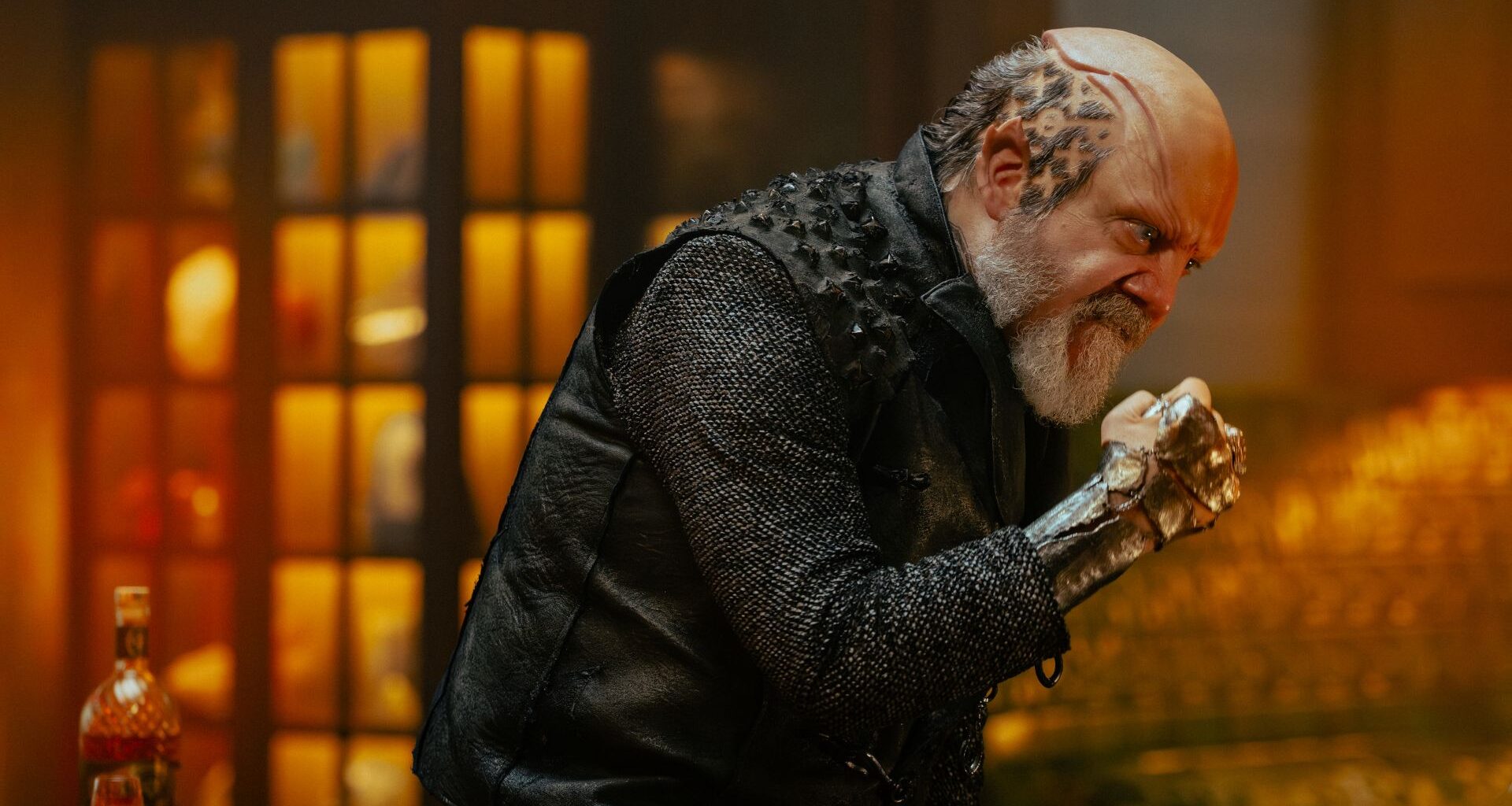 a humanoid alien with x's and o's shaved into the side of his head and a raised cranium makes a fist and an angry face