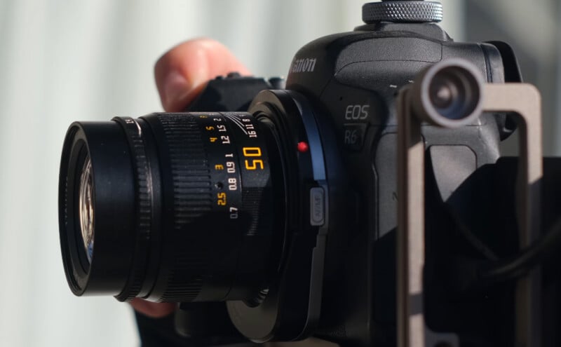 Close-up of a person holding a black Canon EOS R6 camera with a 50mm lens, showing the lens markings and part of the user's hand adjusting the camera.