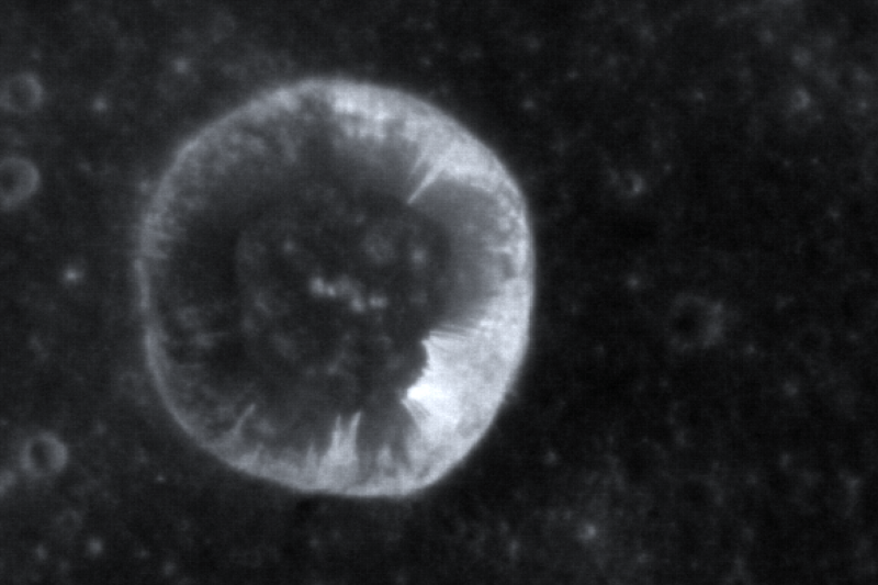 A deep circular crater with white streaks running from the rim down the crater walls.