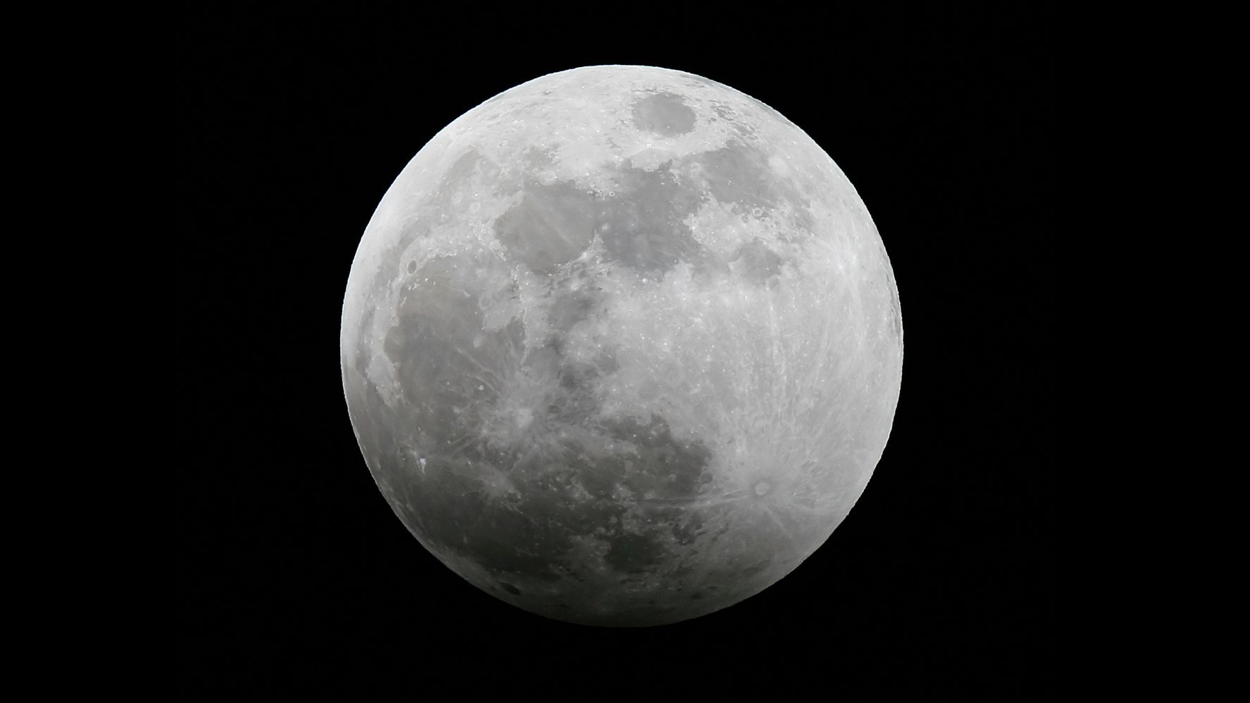 A photo of a full moon against a black sky with its lower section subtly shadowed during an eclipse.