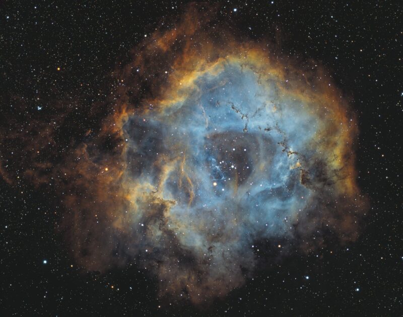 A large, spherical and hollowed-out cloud of yellow and blue gas, with a multitude of immersed stars.