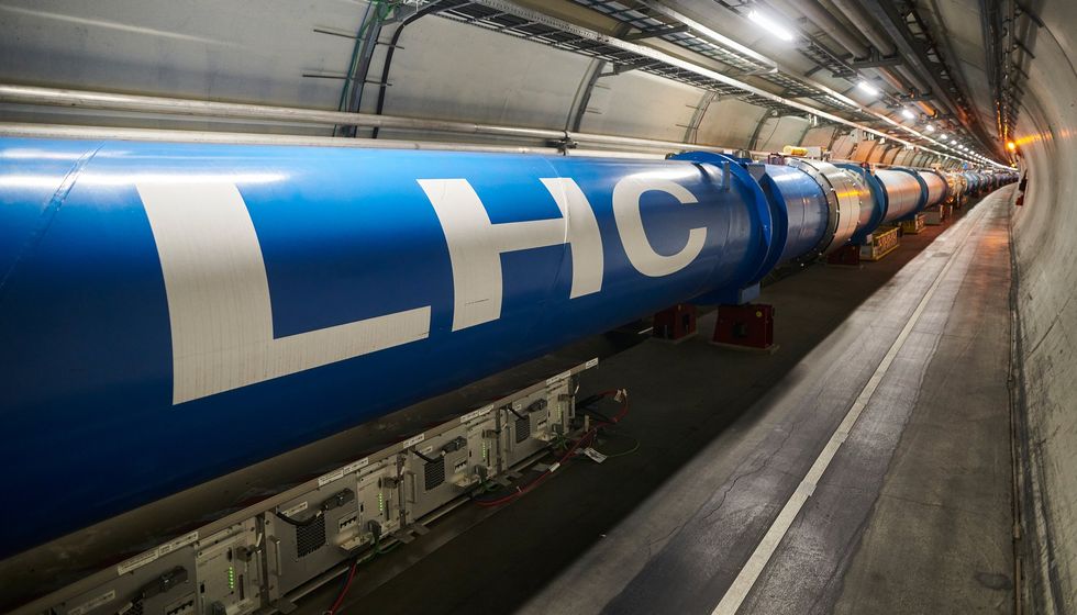 A long blue accelerator tube marked \u201cLHC\u201d runs through an underground tunnel.