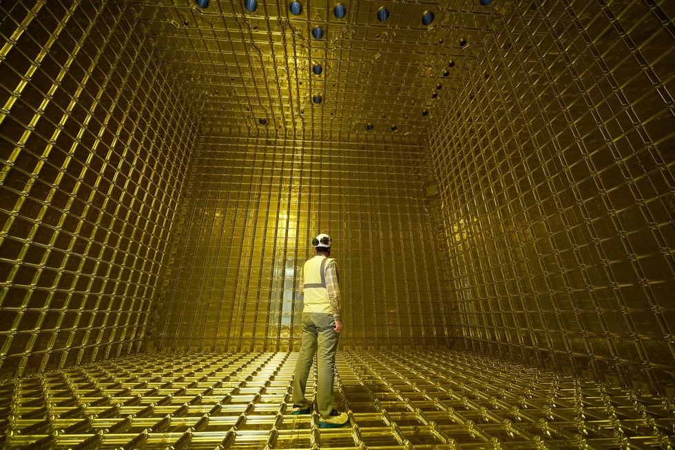 A person stands inside a room that has gold-colored grids covering the floor, walls, and ceiling.