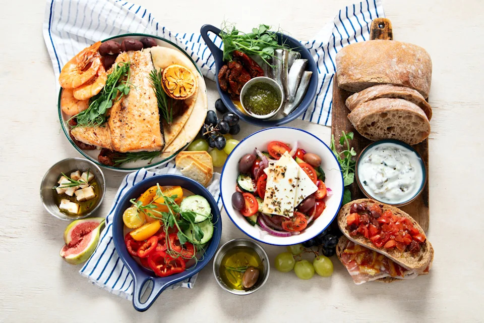 Greek food background. Fsh, pita, greek salad, tzatziki, feta, olives. Traditional different greek dishes set on a light  background. Top view.