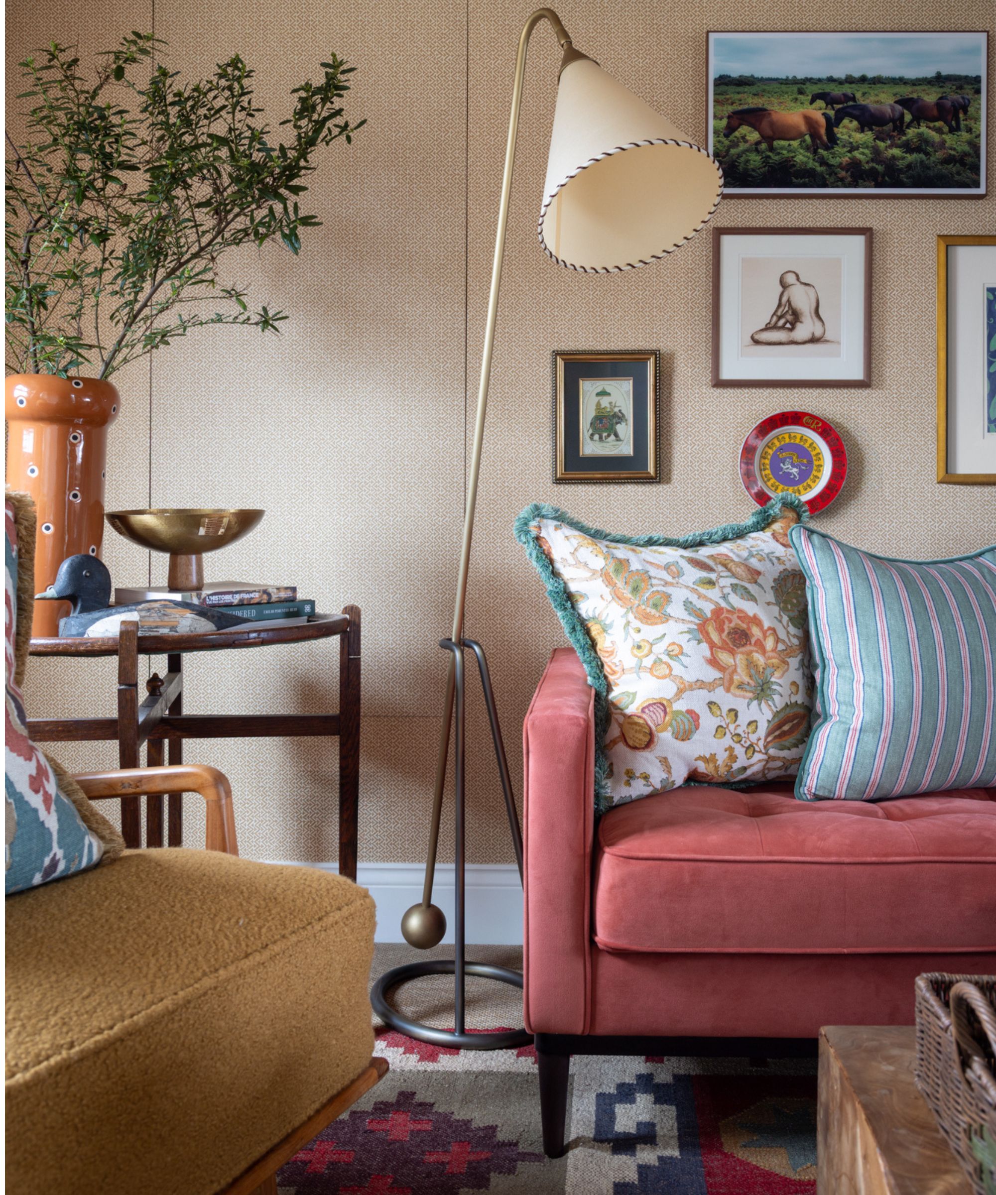 a cozy soft pink english country living room with a pink sofa, gallery wall, and a corner table with a chair, and styled with vases and oddities