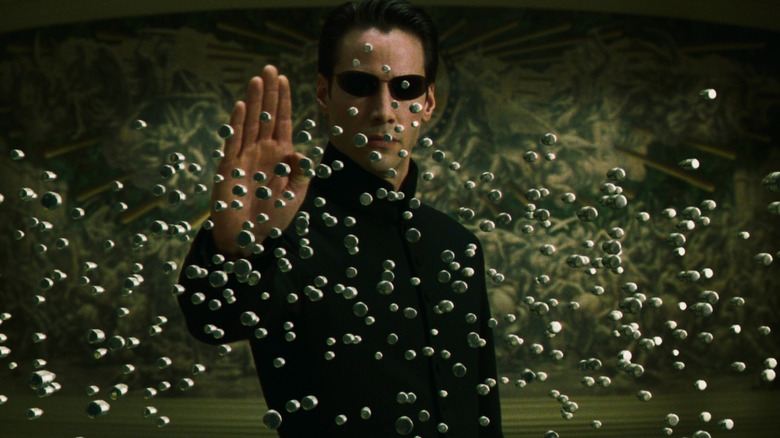 Keanu Reeves as Neo blocking a wall of bullets with his hand in The Matrix