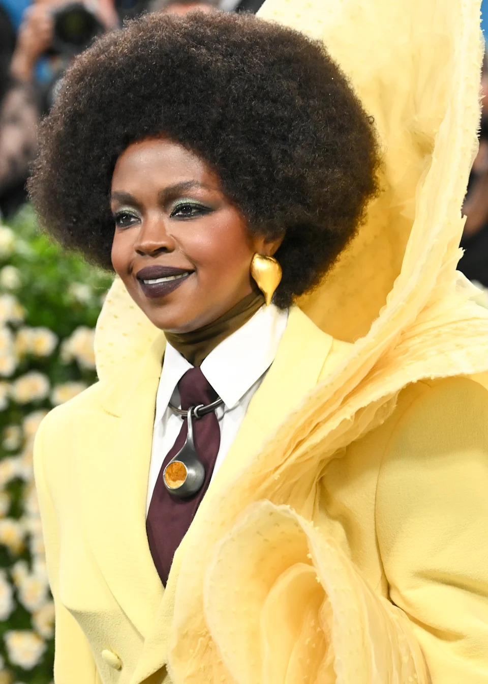 Person in elegant attire with a large, textured overcoat and statement necklace on a formal occasion