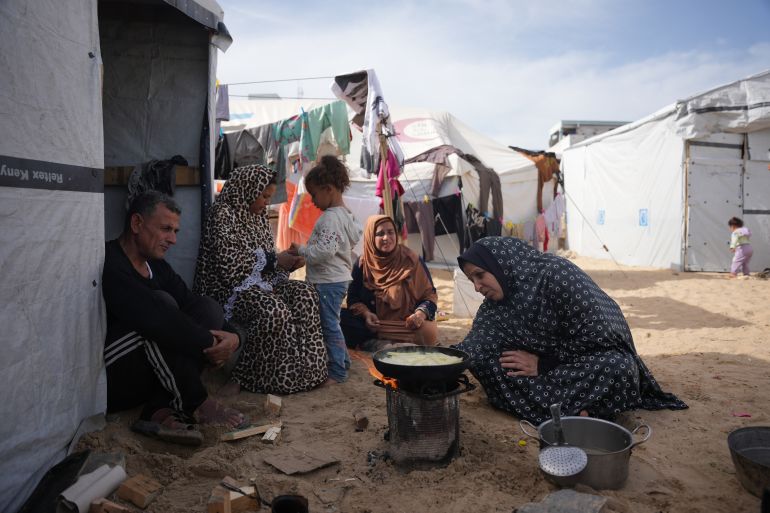 Siham Omran, 54, recently returned from Egypt after completing medical treatment, cooks food over a fire beside her tent in Khan Younis, in the southern Gaza Strip, Saturday, Feb. 7, 2026. (AP Photo/Abdel Kareem Hana)