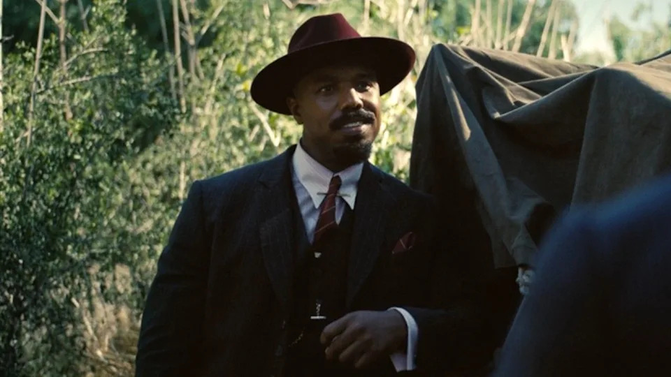 Michael B. Jordan leaning against a truck in Sinners. .