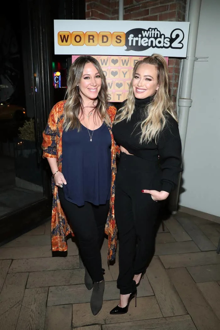 Two women pose at a "Words with Friends 2" event, one in a patterned kimono and the other in a chic black outfit. They are smiling