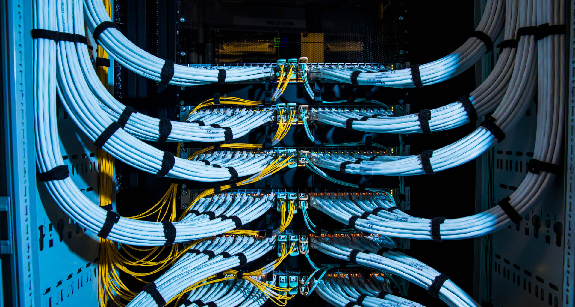 Fiber optic cables, center, and copper Ethernet cables feed into switches inside a communications room