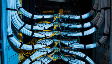 Fiber optic cables, center, and copper Ethernet cables feed into switches inside a communications room