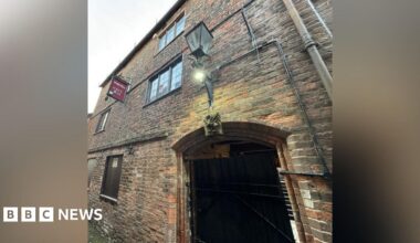 An old gatehouse in a town centre, a three-storey brick building with a large arch.