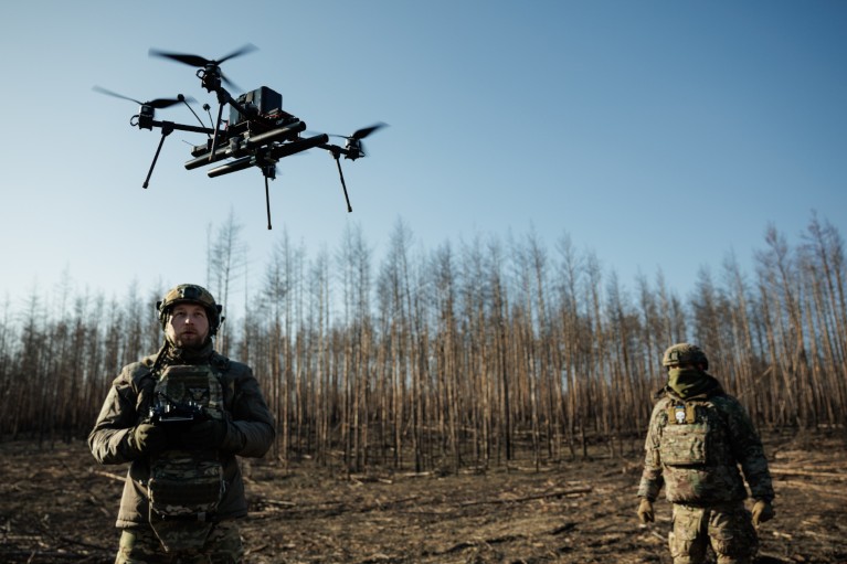 A Ukrainian soldier is seen flying a drone with another soldier behind him.