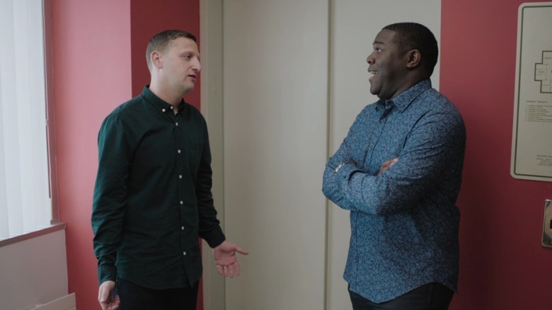 Tim speaking while Sam laughs with his arms crossed on Detroiters S1E9