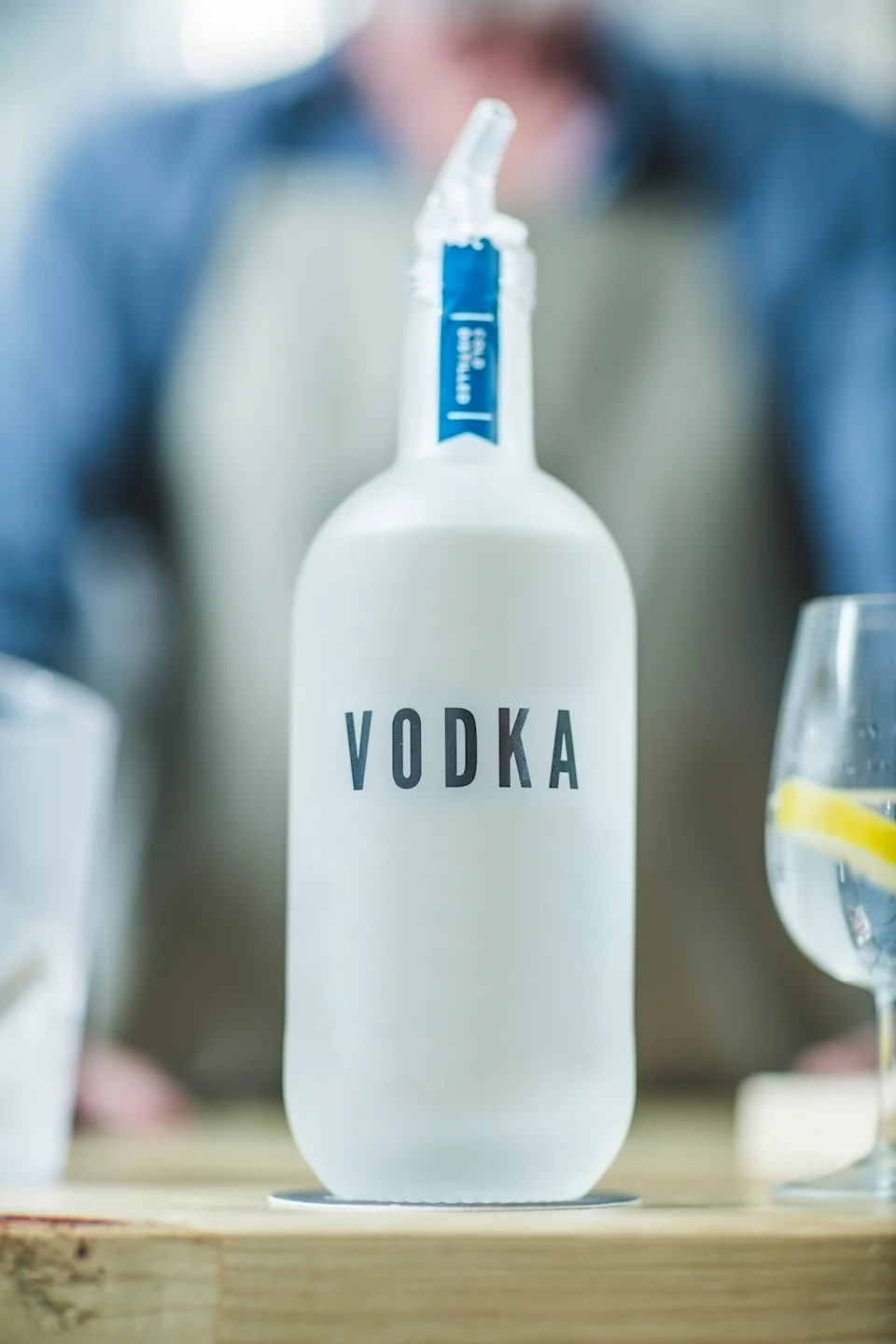 Frosted vodka bottle on a bar counter with a drink nearby, garnished with a lemon slice