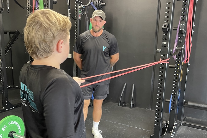 Nine-year-old Deadlift World Record holder Jackson Mackay warming up using a band, supported by his coach Joshua Hodges. 