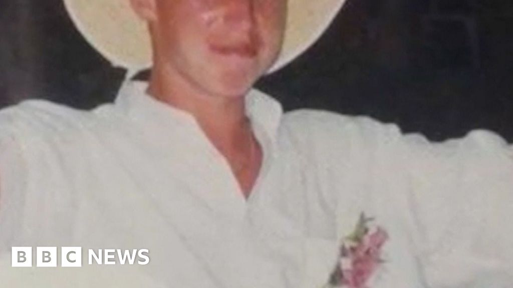Young man wearing a white outfit and a wide brimmed white hat smiling to camera