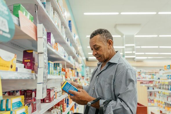 Elderly man looking at medications on a pharmacy shelf.