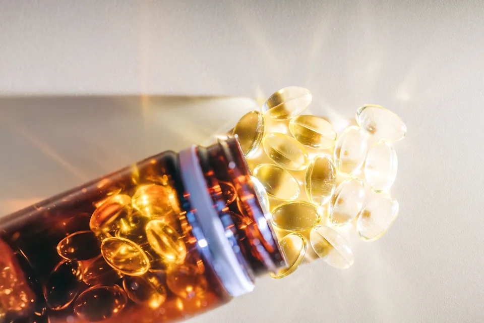 Golden vitamin d pills spilling from brown bottle onto brightly lit surface