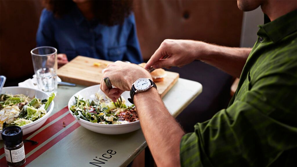 A person wearing a watch eats a bowl of Mediterranean style salad