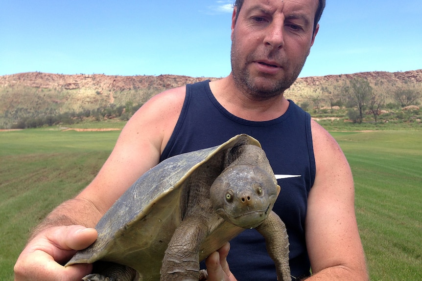 A man in a dark singlet holds a turtle.