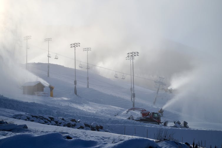 Several machines pump out sprays of snow across a slope.