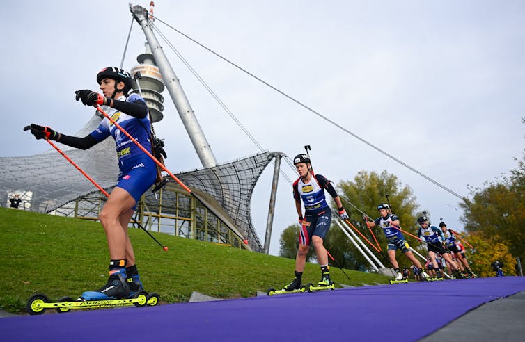 Athletes race on short skis on wheels.