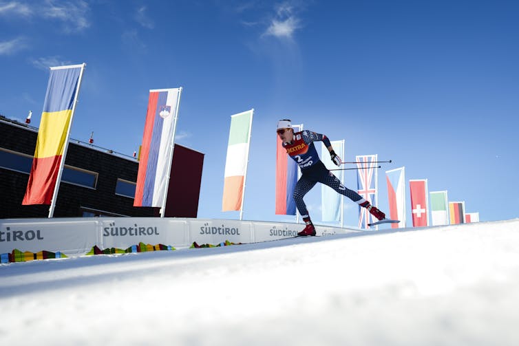 A male skier races down a slick track with flags flying along the wall beside him