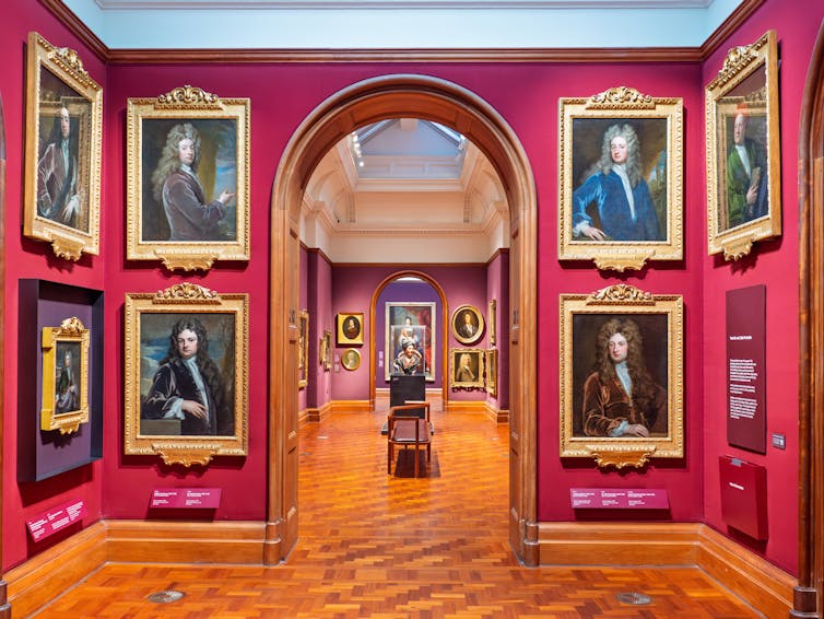 Portraits hung on the walls of a red gallery room