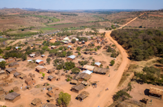 A village seen from the sky, with less than 100 houses on dry red sand and a few bushes here and there