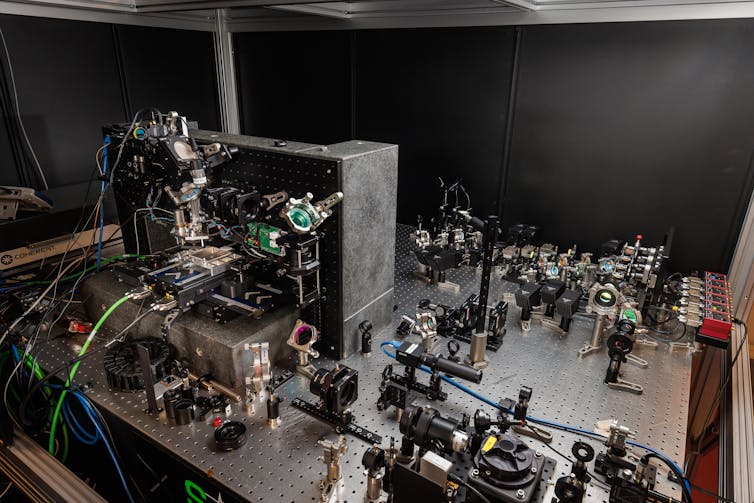 Photo of a lab bench covered in lasers and lenses.