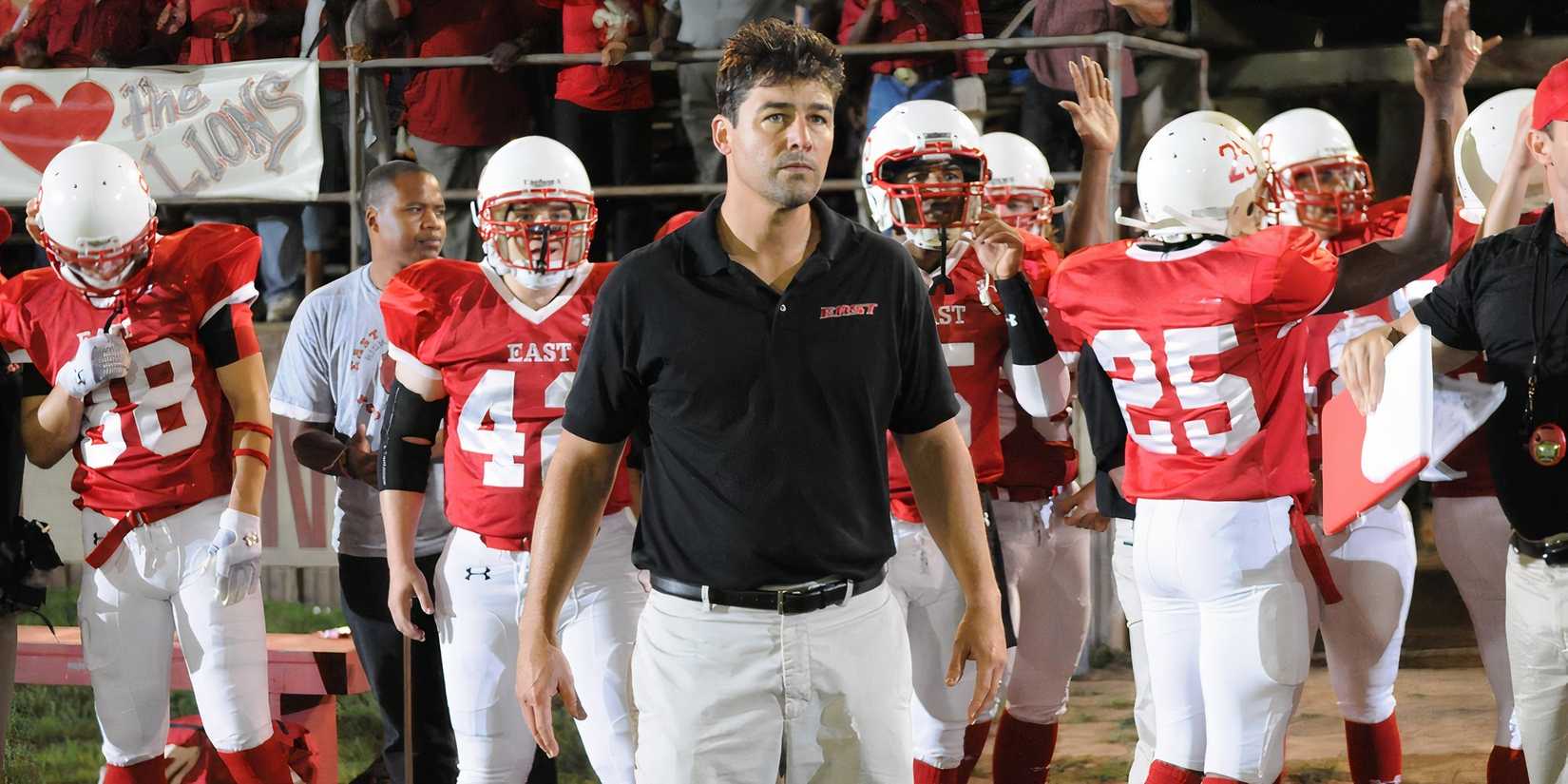 Kyle Chandler as Coach Taylor with players on the sideline at a football game on Friday Night Lights.