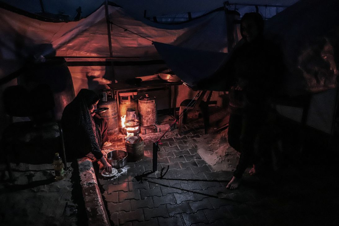 A displaced Palestinian woman prepares food over a fire inside a makeshift shelter near Gaza Seaport in the western part of Gaza City on January 6, 2026.