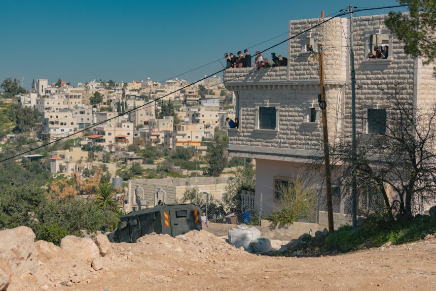 Palestinians watch from balconies as an Israeli military vehicle drives through the village of Beit Awwa near Hebron, in the occupied West Bank.