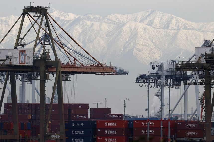 Shipping cranes stand above shipping containers at the Port of Los Angeles, with snow-covered mountains beyond, on Friday.
