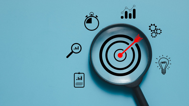 Magnifying glass focusing on a target with an arrow, surrounded by different icons.