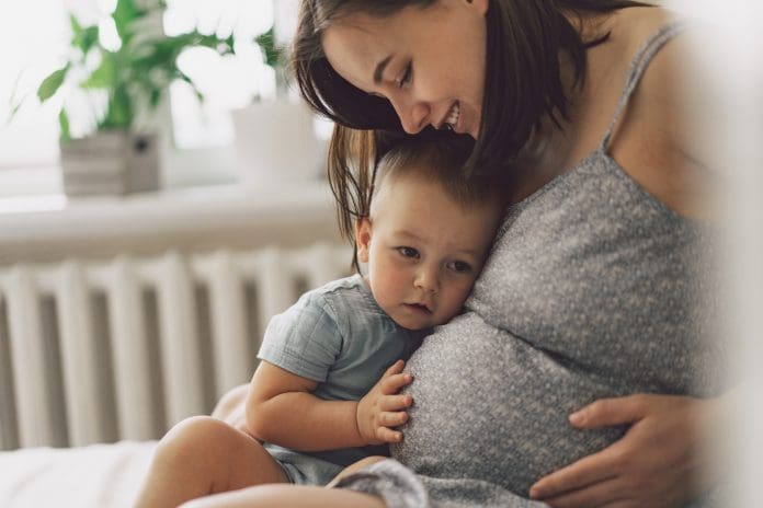 Young woman with her first child during second pregnancy. Motherhood and parenting concept. Toddler boy and mom. Happy family expecting for baby.