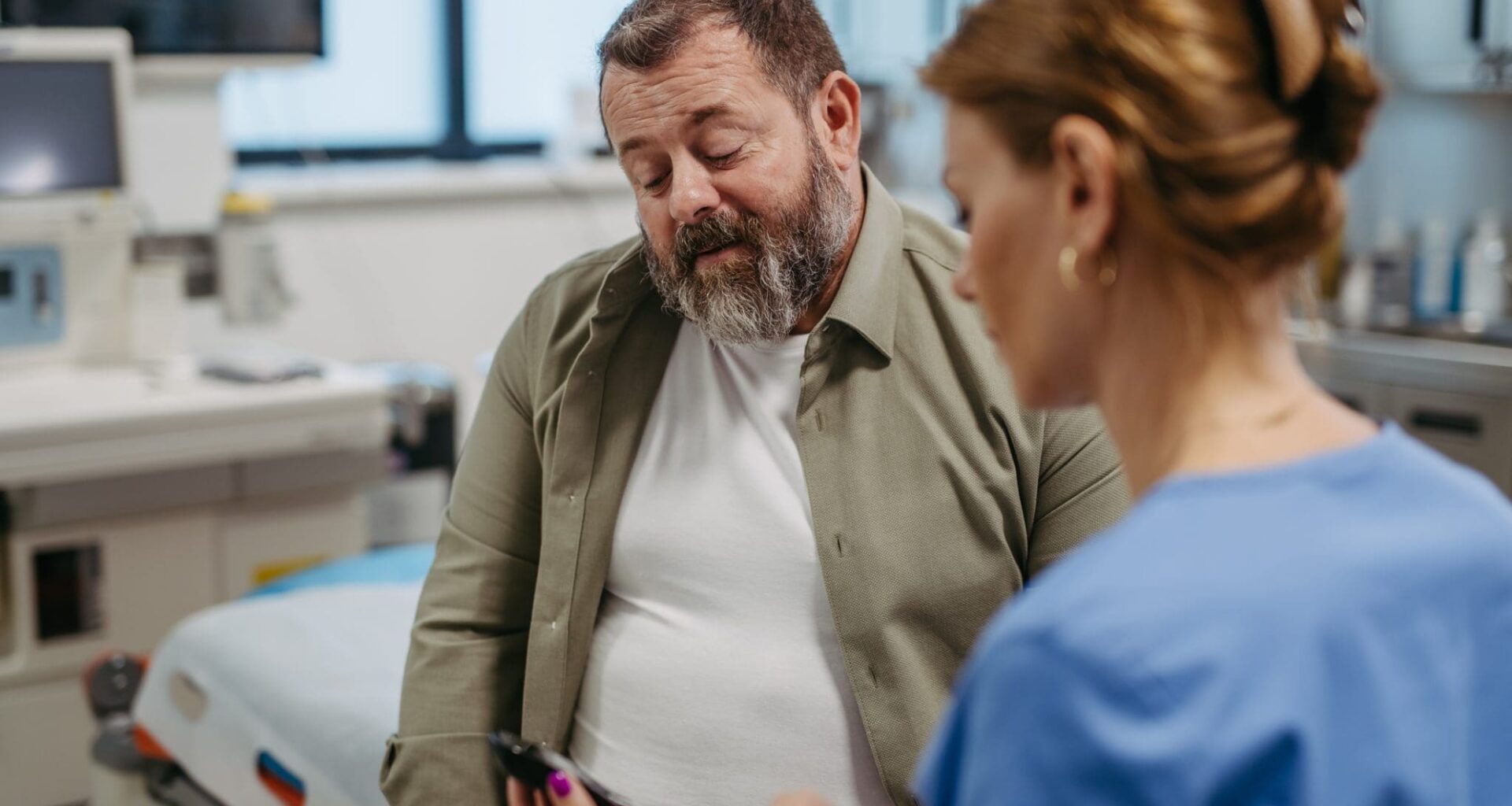 Doctor checking blood glucose level using a fingerstick glucose meter, waiting for results from glucometer. Obese or overweight man at risk of developing type 2 diabetes. Concept of health risks of overwight and obesity.