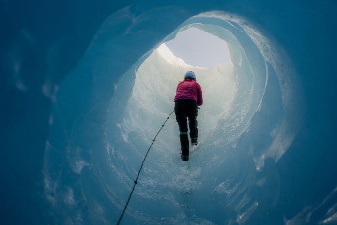 Scientist wearing crampons is climbing a rope while ascending through a stunning deep blue ice cave within a massive glacier