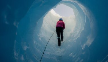 Scientist wearing crampons is climbing a rope while ascending through a stunning deep blue ice cave within a massive glacier
