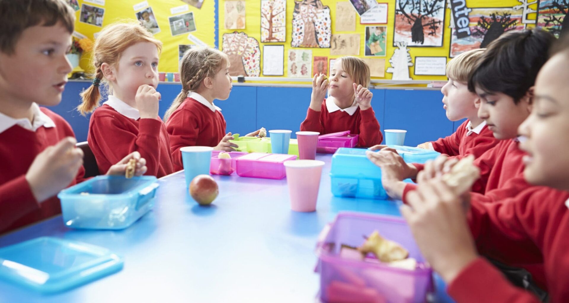 Schoolchildren Sitting At Table Eating Packed Lunch
