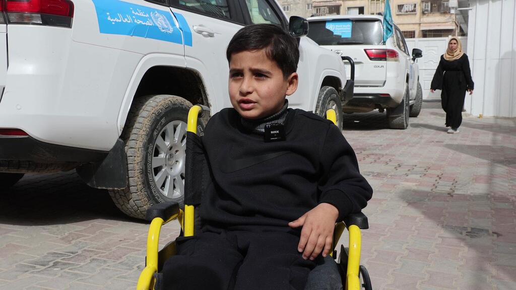 A young boy in a wheelchair is being prepared for transport at Al-Amal Hospital in Gaza, affiliated with the Palestinian Red Crescent Society.