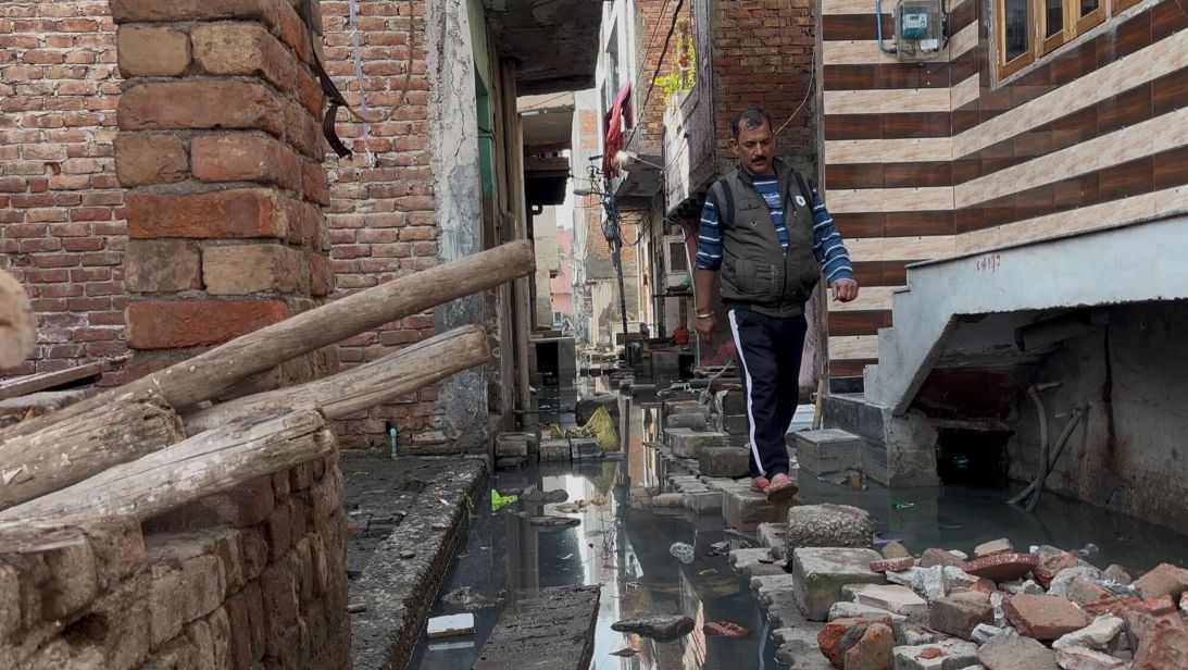 Ravinder Kumar uses stepping stones to cross water outside his home in Sharma Enclave, Delhi.