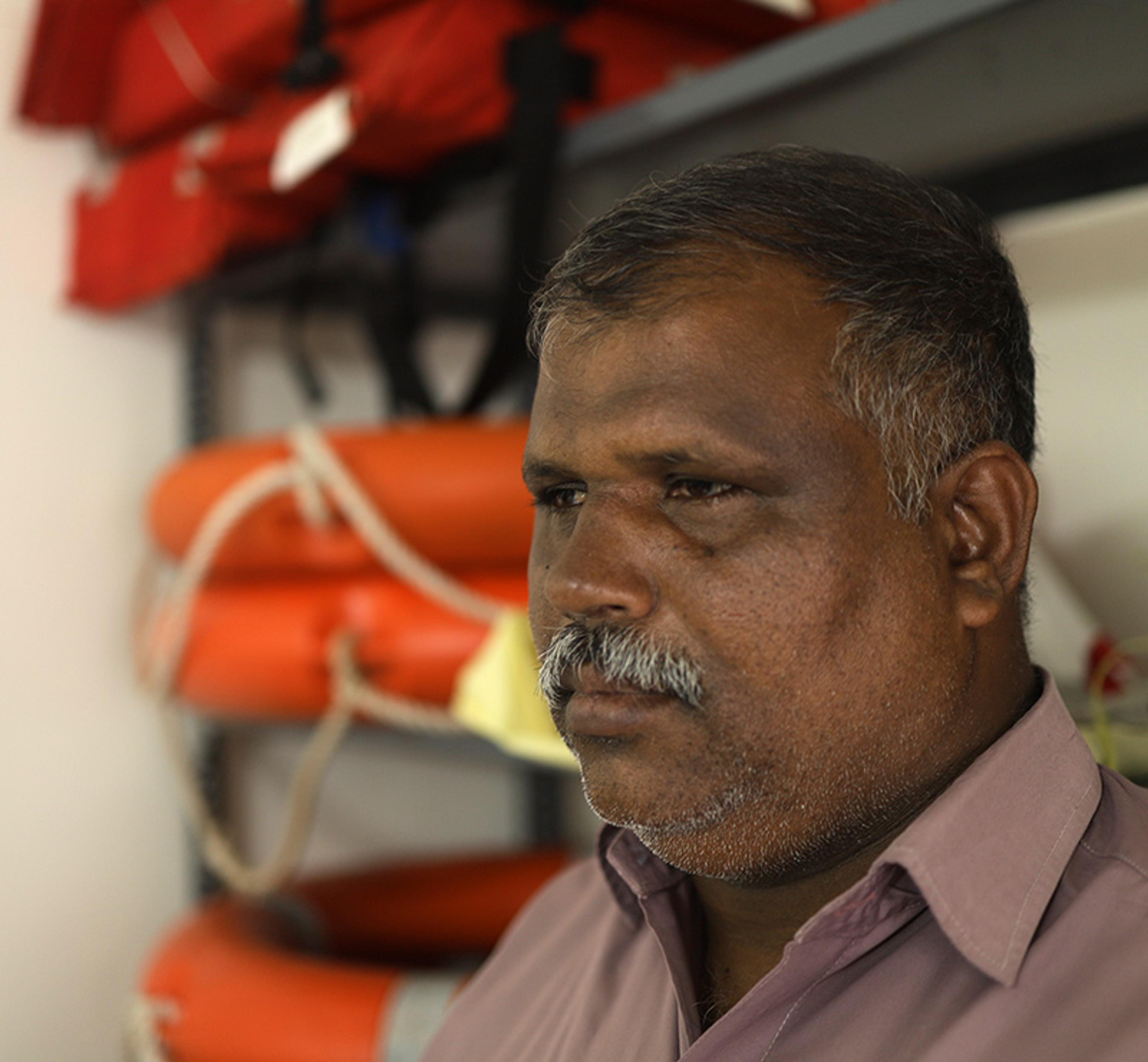 Photo of a man in a purple shirt standing by shelves with lifejackets and lifebuoys in the background.