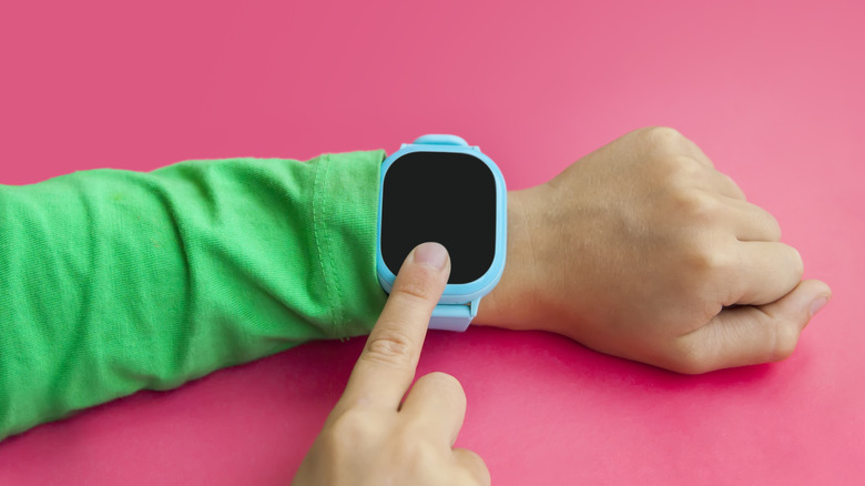 A close-up of a child touching a smartwatch on their wrist.