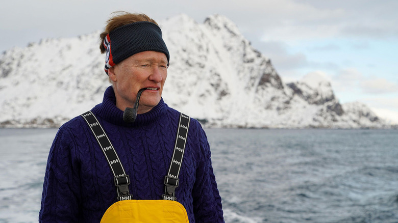 Conan O'Brien wears a purple sweater and black headband while holding a pipe in his mouth with a glacier behind him in "Conan O'Brien Must Go"
