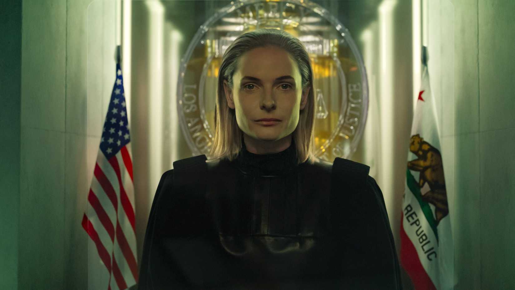 Judge Maddox (Rebecca Ferguson) sitting stoically between two flags in Mercy